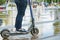 Close-up young person legs in jeans and in sneakers on electric scooter, wet asphalt with puddles after rain