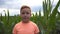 Close up of young red-haired boy looking into camera against the background of corn field at organic farm. Portrait of