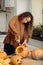 Close up of young woman carving Jack O Lattern from ripe orange pumpkin with knife on her wooden kitchen table. Female