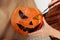 Close up of young woman carving Jack O Lattern from ripe orange pumpkin with knife on her wooden kitchen table. Female