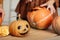 Close up of young woman carving Jack O Lattern from ripe orange pumpkin with knife on her wooden kitchen table. Female