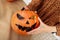 Close up of young woman carving Jack O Lattern from ripe orange pumpkin with knife on her wooden kitchen table. Female