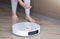 Close-up of young woman connecting smartphone to robot vacuum cleaner to do housework