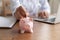 Close up young woman doctor putting coin into piggy bank