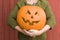 Close-up of young woman holding a pumpkin jack-o-lantern outdoors in the fall with a red barn in the background. Fun rural,