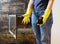 Close up of young woman in jeans, yellow gloves is cleaning the fireplace. Modern fireplace with glass