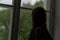 Close up of young woman looking out window in unlit room. Female silhouette observing through window.