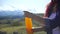 Close-up of young woman opens bottle of orange juice on the background of mountains. 4 k