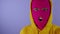 Close up of young woman in pink balaclava and yellow hood grimacing face on purple background. Crazy female in mask