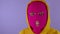 Close up of young woman in pink balaclava and yellow hood squints and shows her teeth on purple background. Unknown