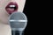 Close up of a young woman with red lips singing to the microphone isolated on black background