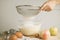 Close-up young woman`s hands pourring milk, making pie, cake. Female cooking dough for pie on wooden table. Preparring