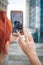 Close-up of a young woman with short red hair walking around the city, taking pictures on a mobile smartphone