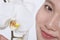 Close up of young woman smiling and a beautiful white flower, half face showing, studio shot