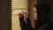 Close up of young woman watching through window blinds at home. Portrait of curious female observing through window