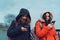 Close up of young women browsing smartphone in city park. Pretty females in hoods using mobile phone.