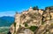 Close view of clifftop Varlaam monastery and rocky slopes of Meteora valley lit by morning sun. Village and mountains