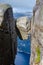 Close view of a Kjeragbolten rock with a blue fjord Lysefjorden in the background way under