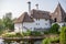 A close view of a structure with an authentic roof with white walls, smokers and a spire at the top. House by the river