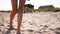 Close view of tanned woman legs and feet walking on sandy beach to the sea on sunny day. Slim pretty girl goes by the