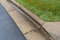Close view of water draining alongside a concrete curb separating green grass from wet asphalt road surface