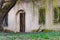 Closed arch door and window under willow tree branches with young leaves. Backyard entrances to abandoned Catholic church of the