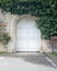 Closed arched white wooden door surrounded by green leaves on old grunge stone wall