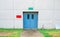 Closed blue door with green and red text box on white concrete wall, grass and walkway