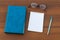 Closed book, eyeglasses, notepad and pen on wooden background