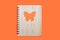 Closed bound notebook with a bamboo cover with a butterfly ornament on an orange background