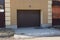 Closed brown gate on the wall of the garage and part of the metal fence on the street