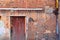 Closed brown painted door, red brick wall with yellow rusty gas pipe with spigot