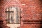 Closed brown red wooden window with rusted metal hinges on a grungy red brick wall