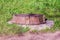 Closed hatch with a concrete base on the green grass in bright sunlight. old manhole side view