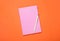 Closed pink notebook and pen on orange background, top view