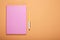 Closed pink notebook and pen on pale orange background, flat lay. Space for text