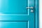 Closed solid wooden door is painted in bright blue with a beautiful metal handle and lock