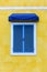 Closed traditional blue Greek window with white frame and blue fabric awning on yellow cement background, copy space