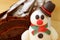 Closed Up an Adorable Snowman Marzipan with Blurred Chocolate Yule Log Cake in Background