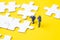 Closed up of miniature people worker or staffs looking at the white jigsaw puzzle pieces on yellow background with copy space,