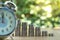 Closed up shot of alarm clock with Coin stacks on green background.