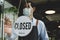 Closed. vintage sign board hanging on glass door with waitress staff wearing protective face mask cleaning and washing mirror wind