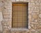 Closed window with wooden shutters and bars with a stone window sill in the old wall of the house