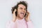 Closep shot of freedom handsome stylish young male with curly hair wearing pink clothes, singing and listening favorite music on