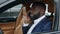 Closeup afro man talking phone at car. Man sitting at front seat at luxury car