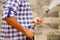 Closeup arms of man wearing square pattern blue and white shirt holding high pressure water gun, pointing towards grey brick wall