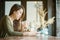 Closeup asian woman reading a book and drinking iced chocolate at the wooden counter desk in coffee shop with happy face on blurre