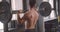 Closeup back view portrait of shirtless muscular caucasian man lifting weights than looking at camera standing in the