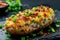 Closeup baked potato stuffed with bacon, green onions and cheddar cheese on black plate