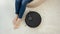 Closeup of barefoot young woman working at home while robot vacuum cleaner doing housework and cleanup. Concept of